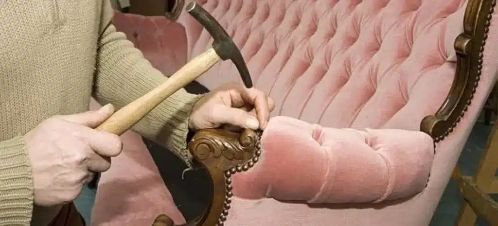 Upholsterer working on a very old sofa during refurbishment, installing decorative nailheads along the frame.