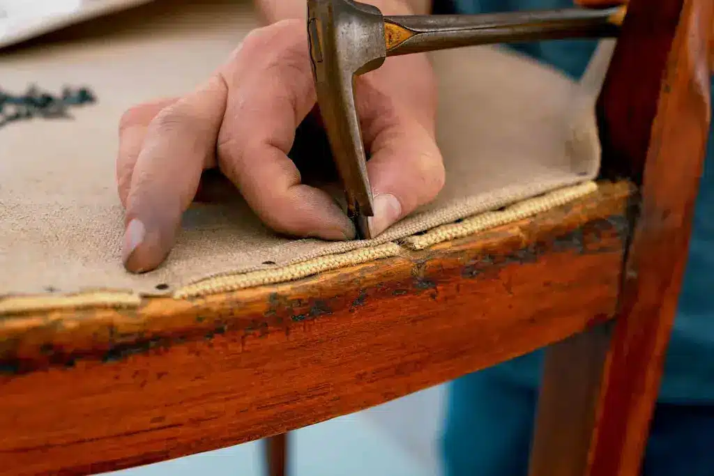 Upholsterer repairing the furniture frame and installing tack nails through the burlap to secure the foundation.